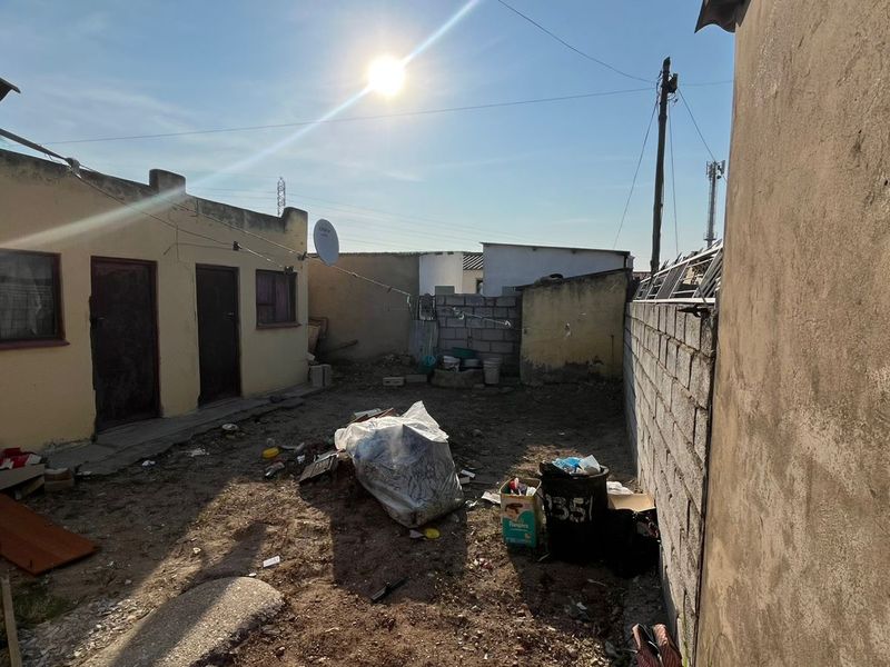 Rear exterior area featuring plastered walls and a concrete block boundary wall, requiring significant maintenance and landscaping to improve the property's outdoor space.