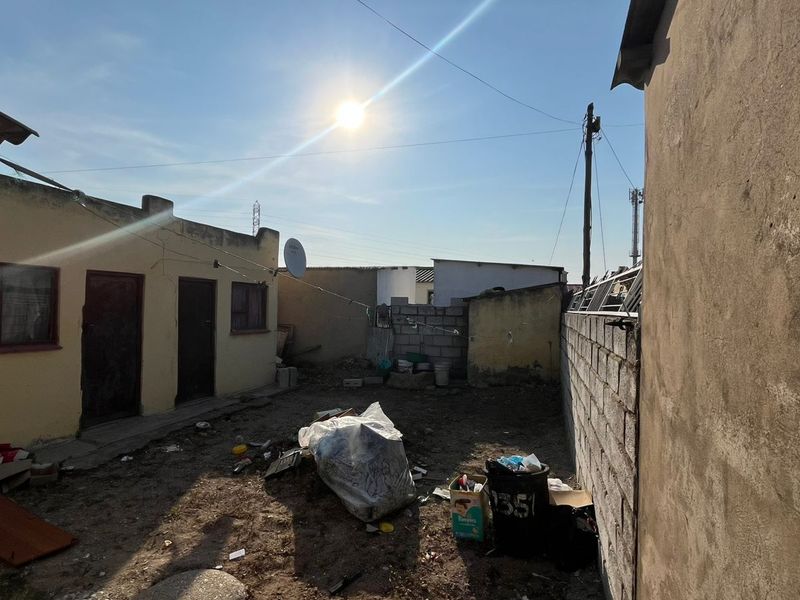 Rear exterior area featuring plastered walls and a concrete block boundary wall, requiring landscaping and maintenance to improve the outdoor space.