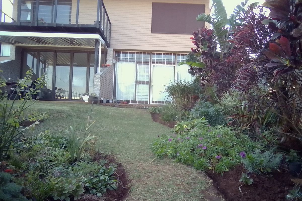 Rear view of the apartment featuring a balcony, sliding glass doors with security bars, and a well-maintained landscaped garden with lawn.
