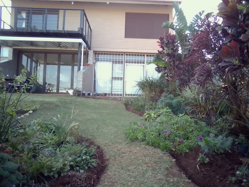 Rear view of the apartment featuring a balcony, sliding glass doors with security bars, and a well-maintained landscaped garden with lawn.