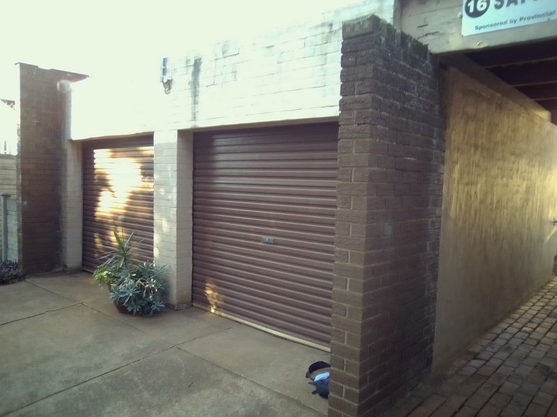 A double garage exterior featuring brown roller shutter doors, brick pillars, and a concrete driveway with a paved side walkway.