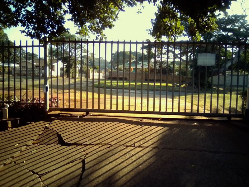 View of the property entrance featuring a metal security gate and a concrete driveway with visible surface cracking.