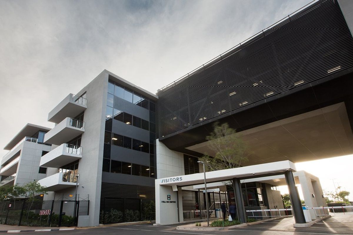 Modern commercial building exterior featuring a visitor entrance, boom gate security, and contemporary architectural design with glass and louvred facade elements.