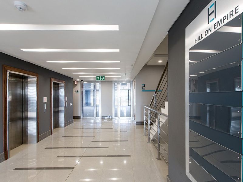 Modern commercial building lobby featuring polished tiled floors, stainless steel elevators, a staircase, and clear directional signage for Hill on Empire.