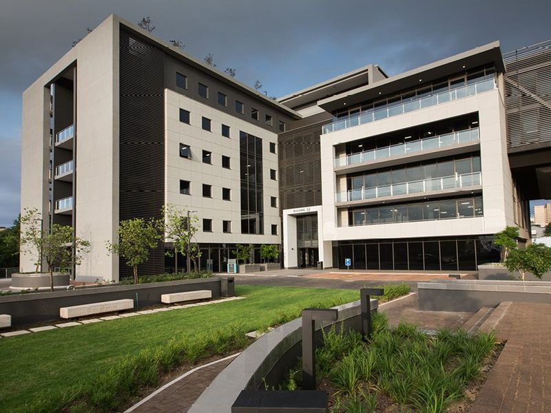 A modern multi-story commercial office building featuring contemporary architectural design, glass balconies, and well-maintained landscaped grounds with paved pedestrian walkways.