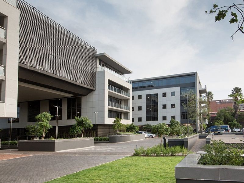 Modern commercial office complex featuring contemporary architectural design, paved driveway, landscaped garden areas, and glass-fronted balconies.