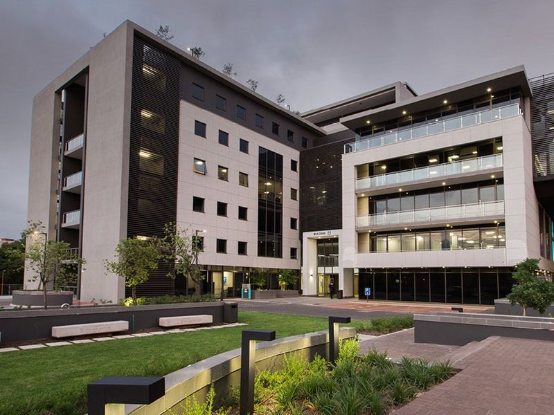 Modern multi-story commercial office building featuring contemporary glass facades, integrated balconies, and well-maintained landscaped grounds with paved pedestrian walkways.