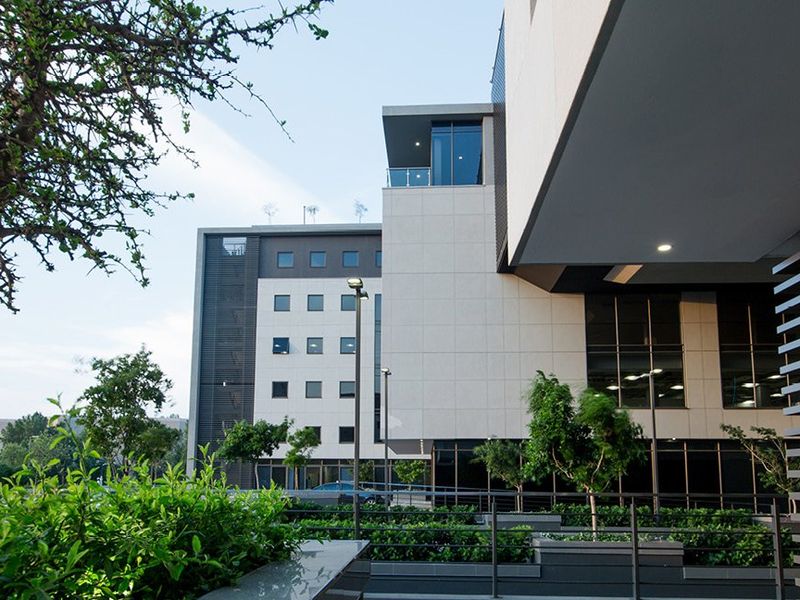 Modern commercial building exterior featuring clean architectural lines, glass balcony balustrades, integrated lighting, and well-maintained landscaped garden planters.