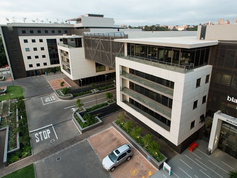Aerial view of a modern commercial office complex featuring multi-story buildings, glass balconies, paved parking areas, and landscaped grounds.