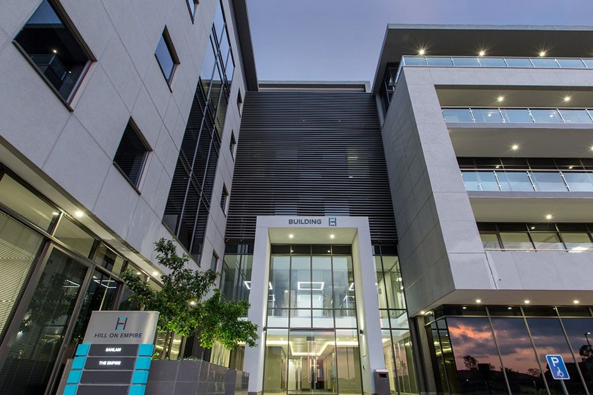 Modern commercial office building facade featuring glass curtain walls, aluminum louvers, and integrated balcony lighting at the main entrance.