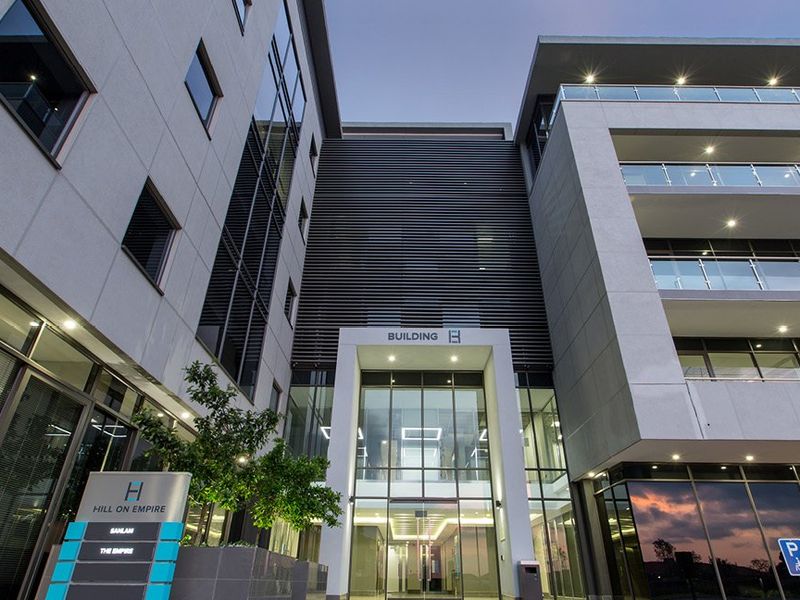Modern commercial office building facade featuring glass curtain walls, aluminum louvers, and integrated balcony lighting at the main entrance.