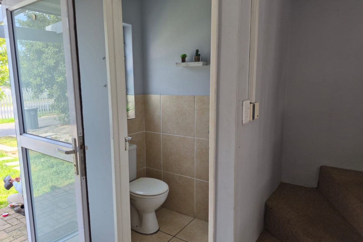 A compact bathroom featuring tiled walls and flooring, adjacent to a glass exterior door and carpeted staircase.