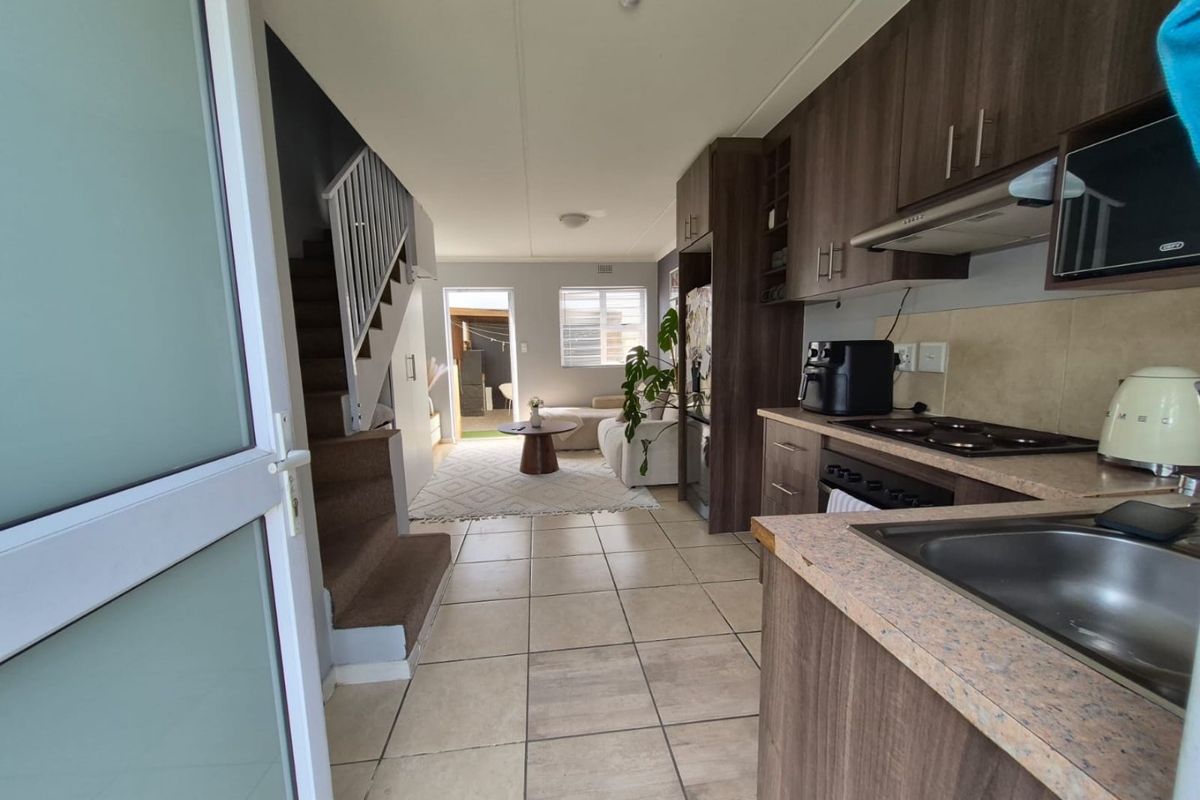 Open-plan living area featuring a functional kitchen with built-in cabinetry, hob, and oven, seamlessly flowing into the lounge space with staircase access.
