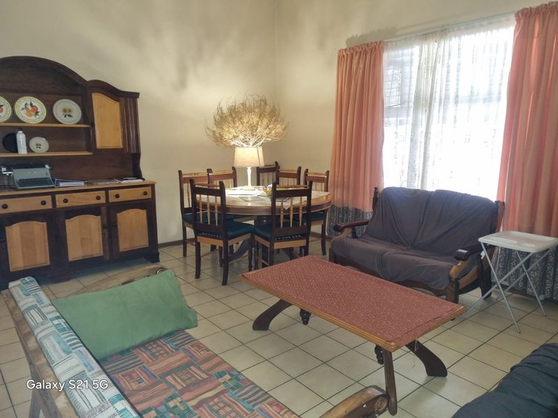 A living and dining area featuring ceramic floor tiles and large windows with curtain rails, offering a functional space for relaxation and meals.