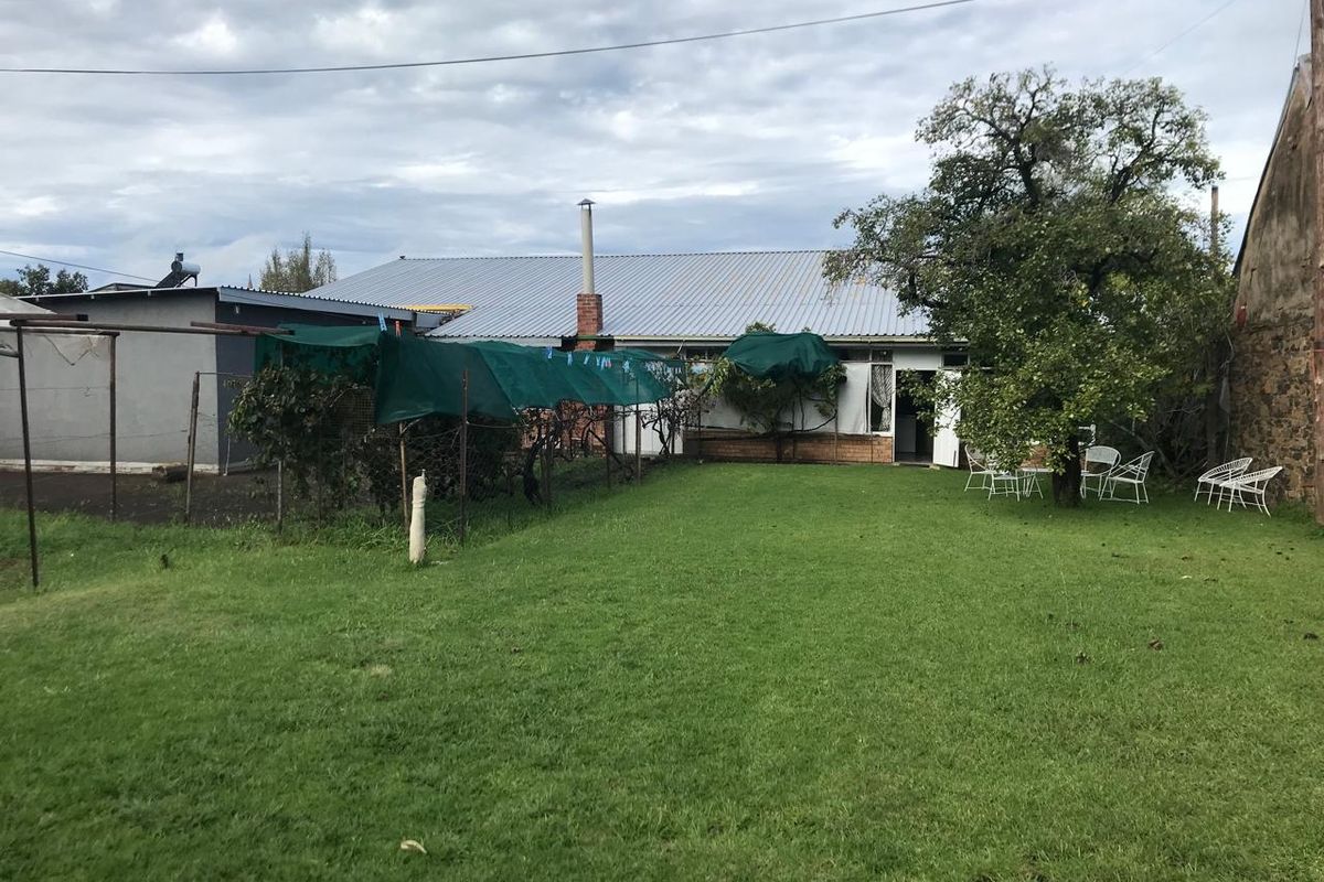 A view of the rear exterior of the house featuring a large lawn, corrugated metal roofing, and a brick chimney.