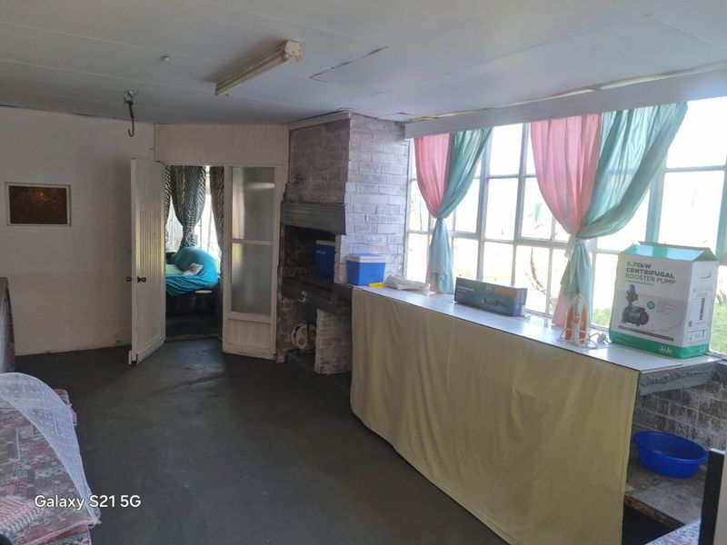 Enclosed patio area featuring a built-in brick braai, large steel-framed windows, and concrete flooring, offering potential for a modern entertainment space.