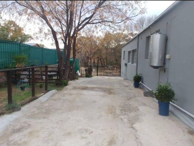 Rear exterior area featuring a concrete driveway, perimeter fencing, and an external geyser mounted on the building wall.