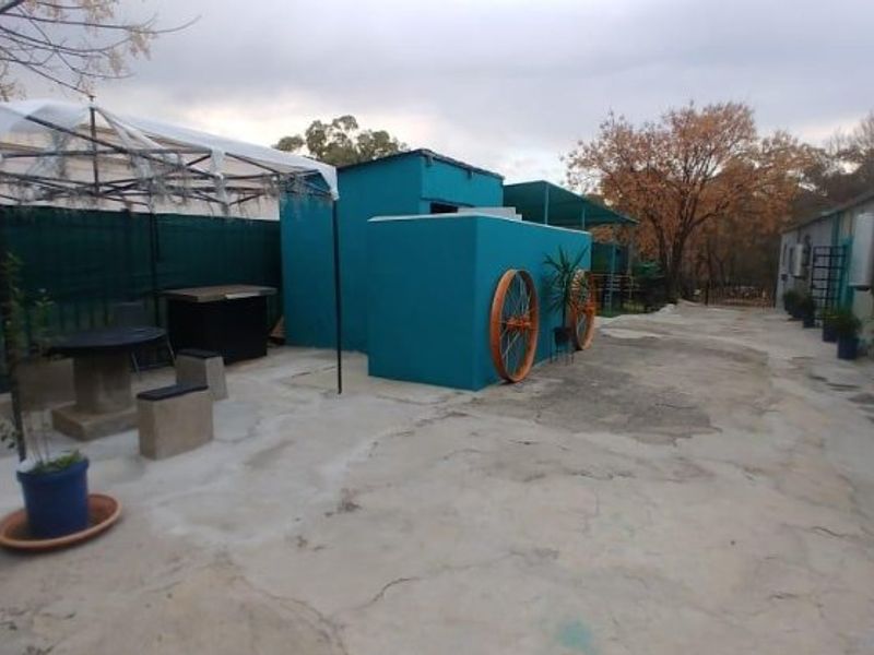 Rear exterior area featuring concrete paving, metal water tanks, and a covered outdoor space with perimeter fencing.