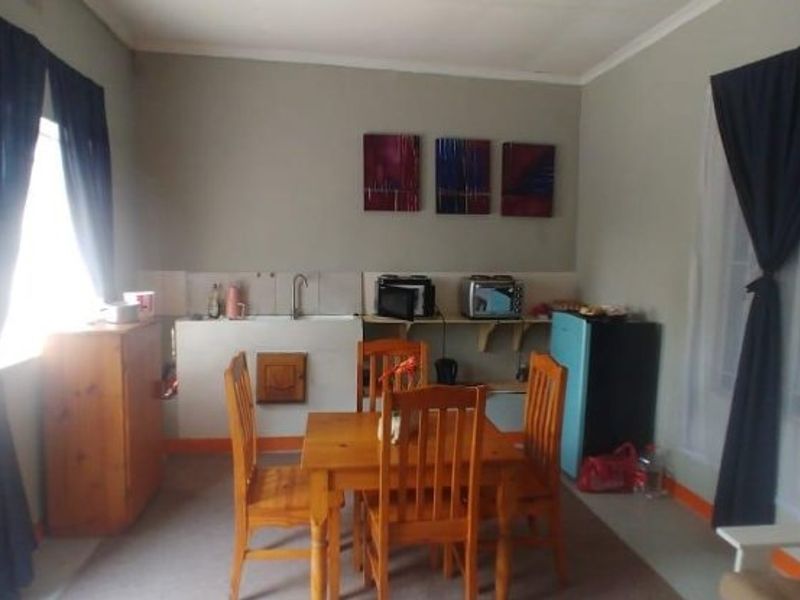 Open plan living and kitchen area featuring a basic sink unit, tiled splashback, and security bars on windows.