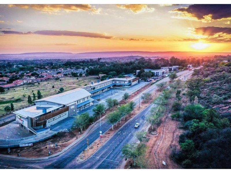 Aerial view of a commercial retail complex featuring a large parking area and road access at sunset.