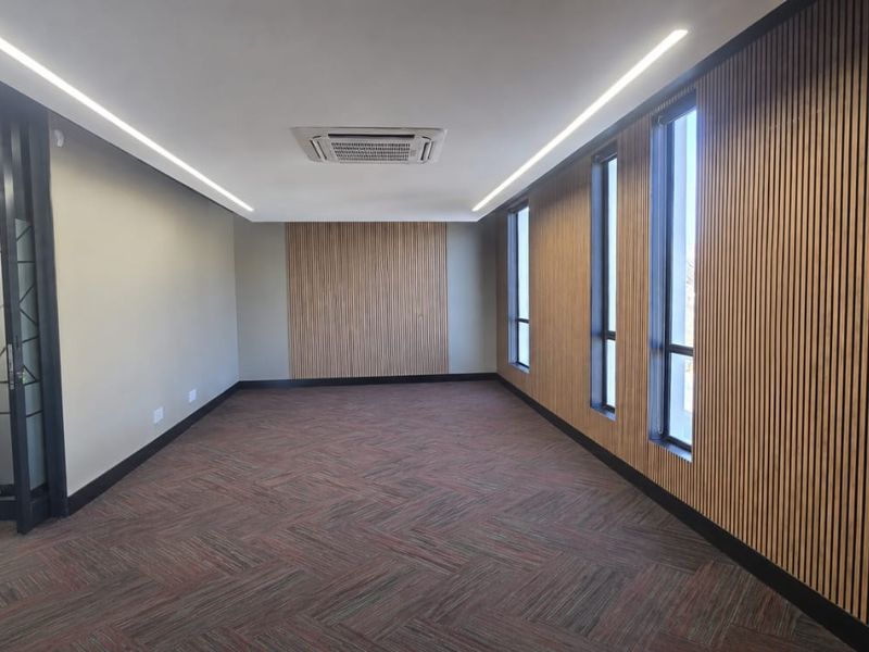 Modern, empty office space featuring timber slat wall paneling, recessed linear lighting, a cassette air conditioning unit, and high-quality herringbone carpet tiles.
