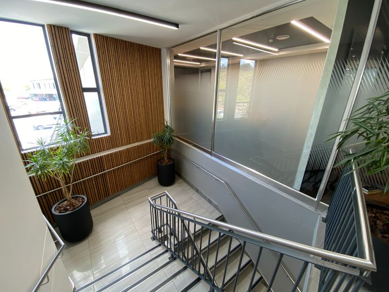 Modern commercial hallway featuring timber slat wall paneling, glass partitions, tiled flooring, and a metal staircase with stainless steel handrails.