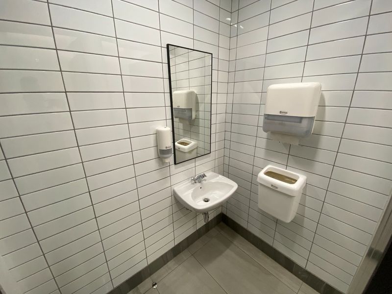 A clean, modern commercial bathroom featuring white subway-style wall tiles, a wall-mounted basin, and essential wall-mounted utility fixtures.