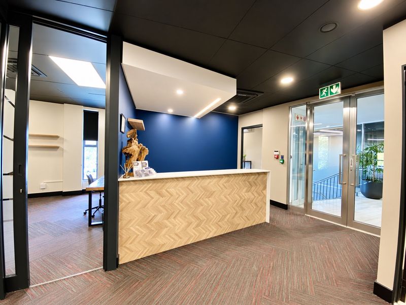 Modern commercial reception area featuring a herringbone-patterned desk, dark ceiling accents, and glass entry doors leading to a stairwell.