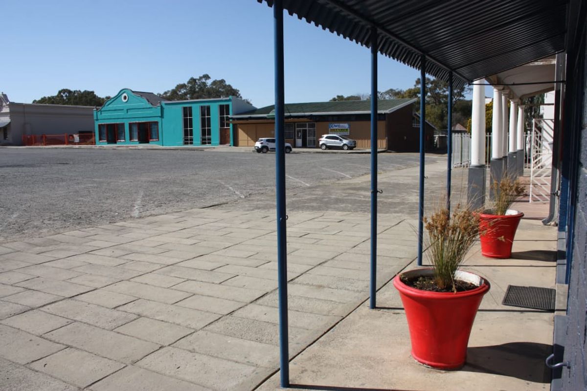 Commercial property frontage featuring a covered walkway, paved forecourt area, and metal awning structure overlooking a shared parking space.