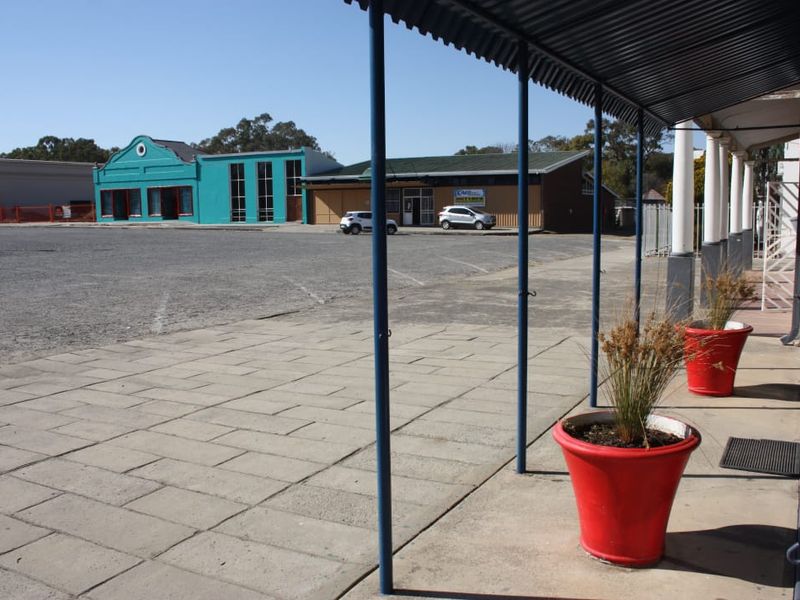 Commercial property frontage featuring a covered walkway, paved forecourt area, and metal awning structure overlooking a shared parking space.