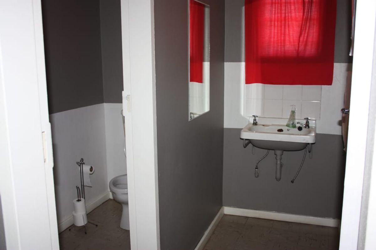 A functional bathroom featuring a wall-mounted basin with tiled splashback and a separate toilet area, requiring cosmetic updates to improve its overall condition.