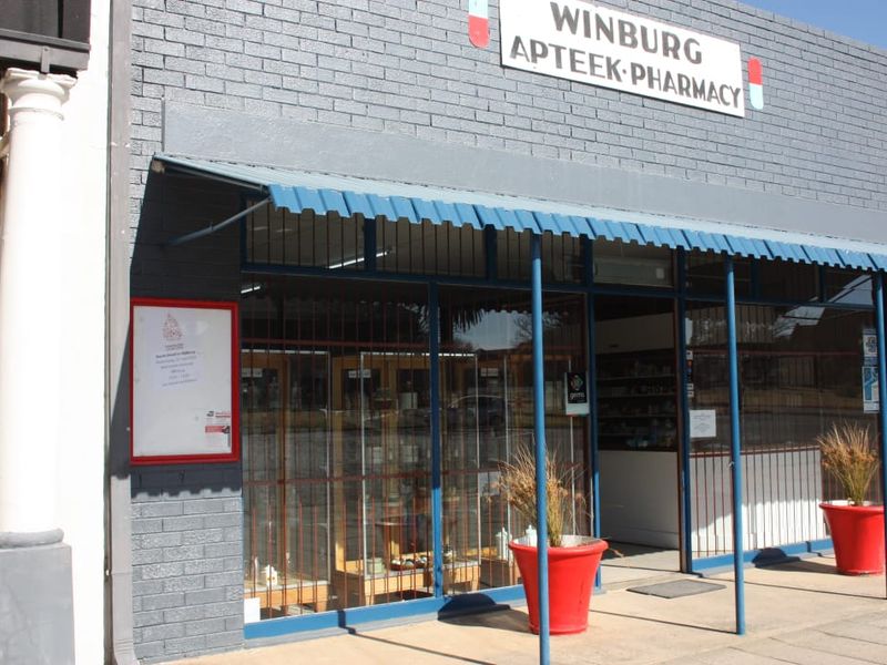 Front facade of a commercial pharmacy building featuring a brick exterior, metal awning, and large glass storefront entrance.