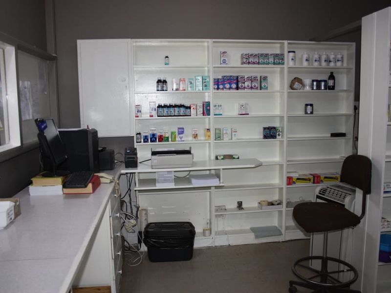 A functional commercial utility or pharmacy prep area featuring extensive built-in white shelving and a laminate workspace.