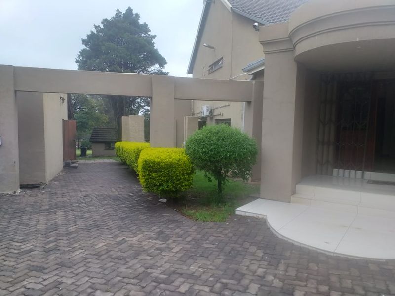Front exterior view of the property featuring a paved driveway, covered entrance area with tiled steps, and established garden hedging.