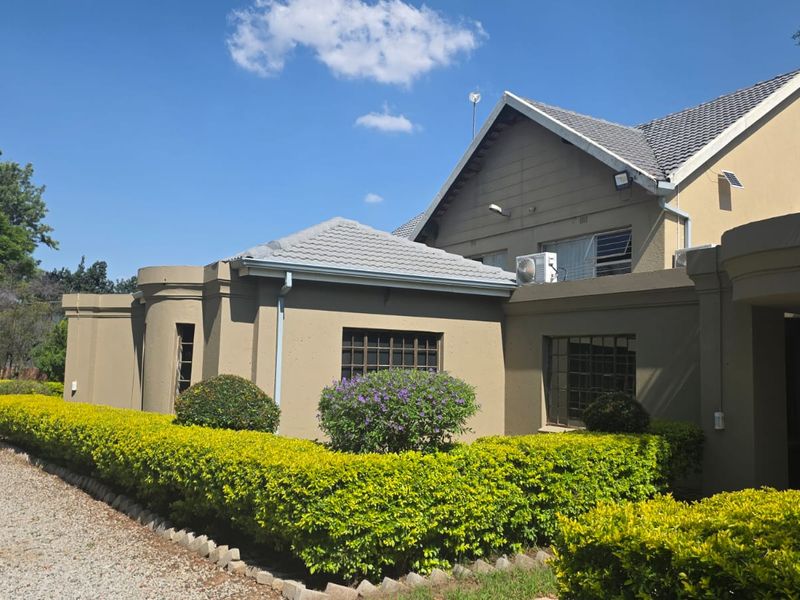 A view of the front exterior of the house featuring a tiled roof, security bars on windows, and well-maintained garden hedges.