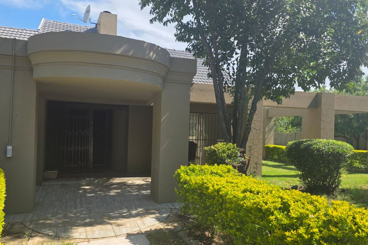 Rear exterior view featuring a covered patio area, concrete structural pillars, and a landscaped garden with established shrubs.