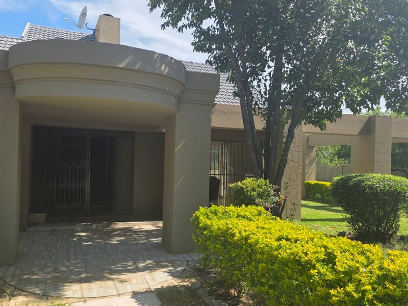 Rear exterior view featuring a covered patio area, concrete structural pillars, and a landscaped garden with established shrubs.