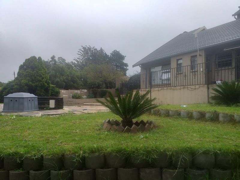 Rear view of the property featuring a tiled roof, elevated patio with wrought iron railing, and a tiered garden with retaining walls.
