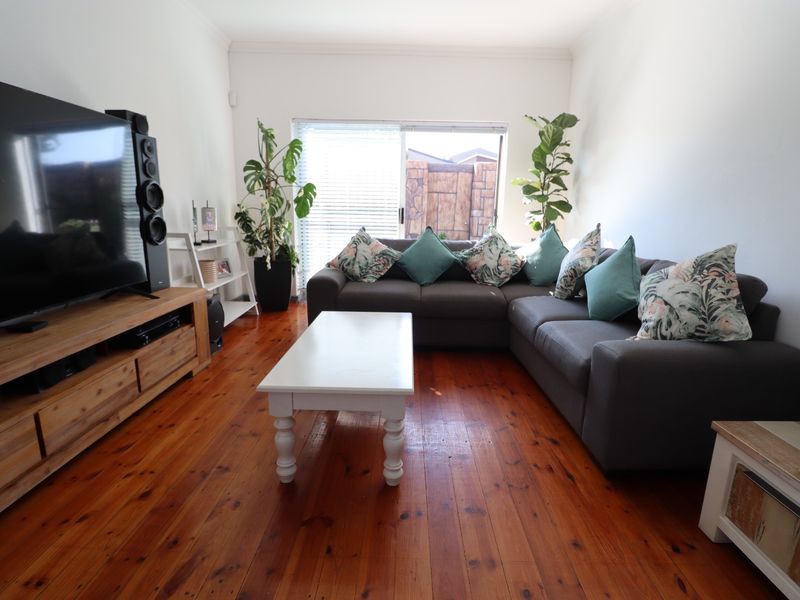 A comfortable living room featuring warm timber flooring and a sliding glass door that provides natural light and access to the outdoor area.