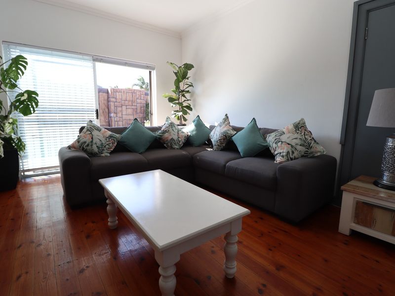 A bright living room featuring polished hardwood flooring, cove molding, and a large sliding glass door providing access to the exterior.