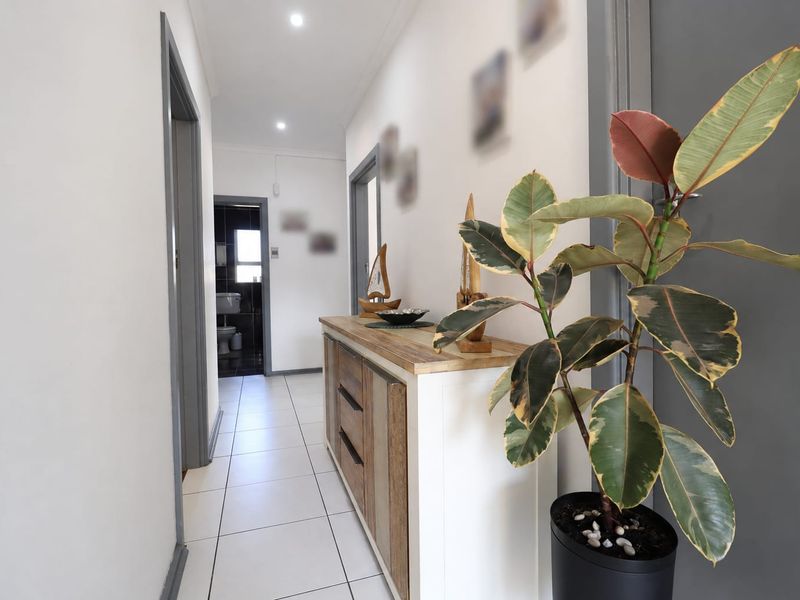 A bright, well-maintained hallway featuring neutral tiled flooring and recessed downlighting, providing access to adjacent rooms.