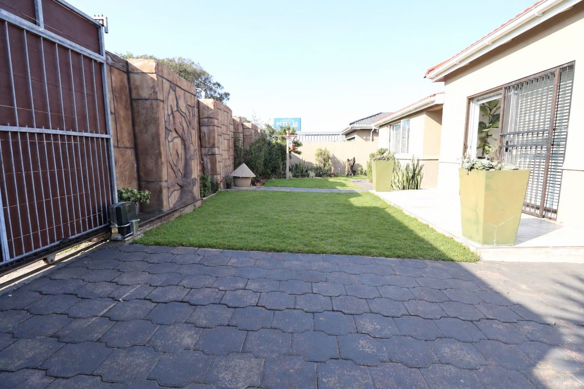 A well-maintained rear garden featuring a paved driveway, a neat lawn, and a decorative boundary wall, providing a private outdoor space.