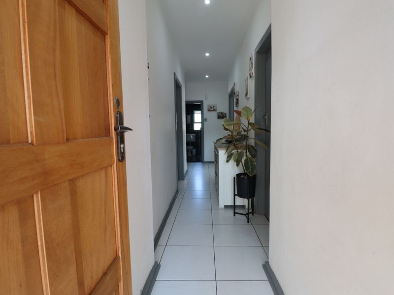A bright hallway featuring tiled flooring, recessed downlighting, and a solid timber entrance door, providing access to various rooms within the home.