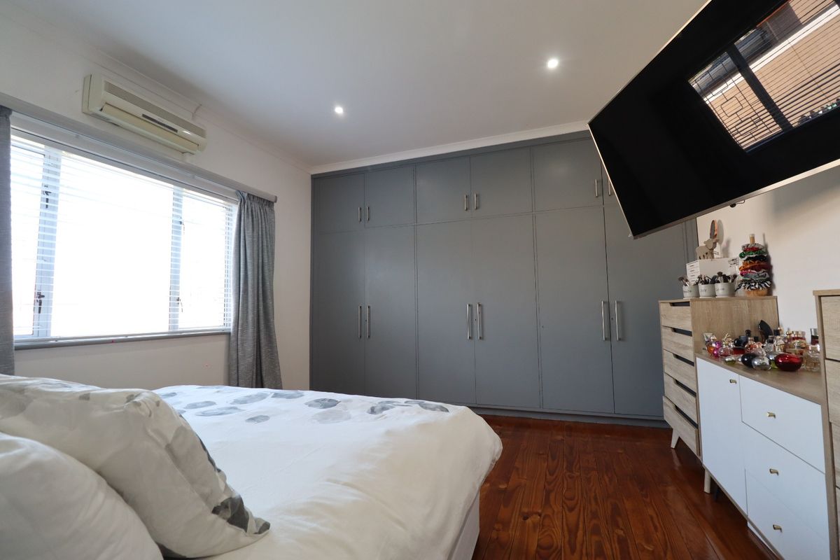 A well-maintained bedroom featuring polished hardwood flooring, extensive grey built-in cabinetry, and a wall-mounted air conditioning unit.