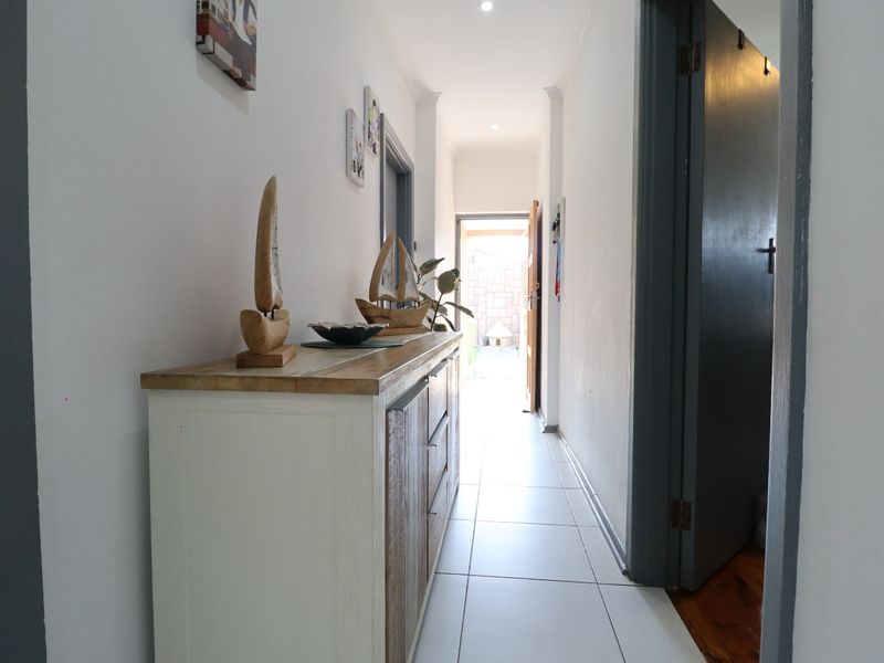 A bright hallway featuring tiled flooring and recessed downlighting, providing access to various rooms and leading towards an exterior exit.