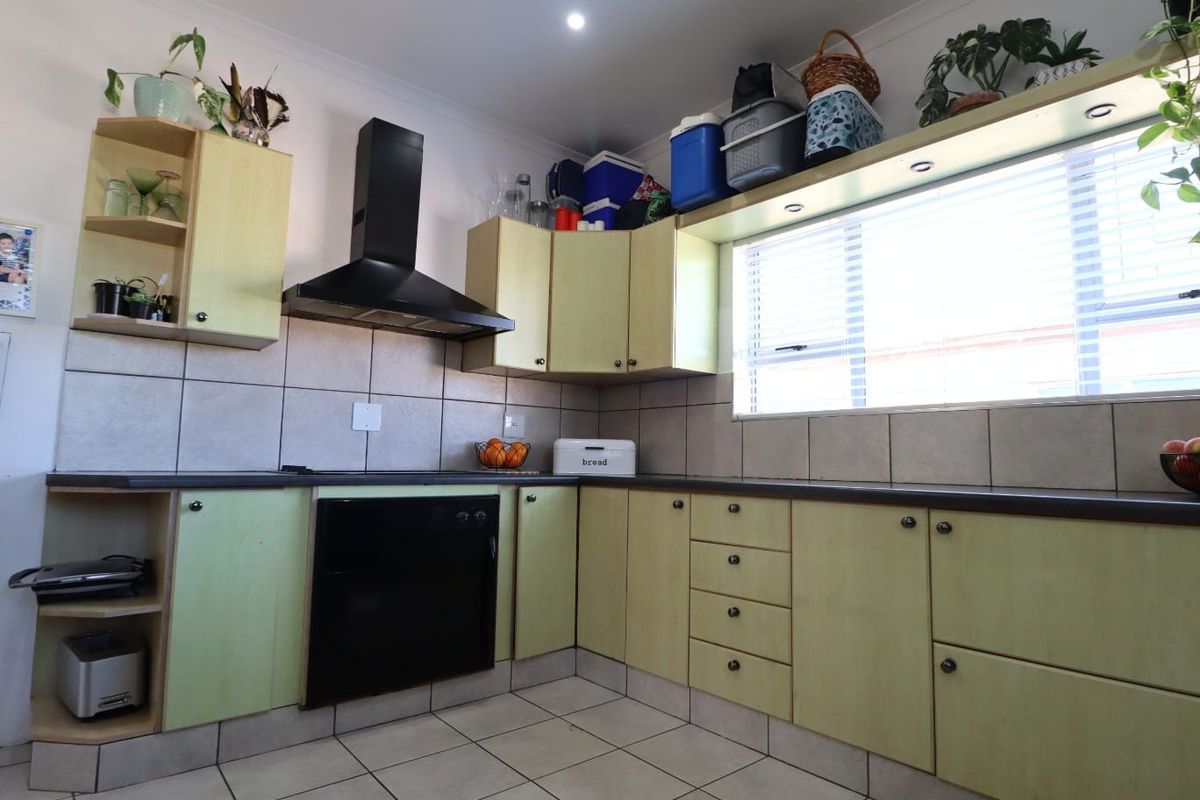 A functional kitchen featuring built-in cabinetry, a black extractor fan, integrated oven, tiled backsplash, and tiled flooring with natural light from a window.