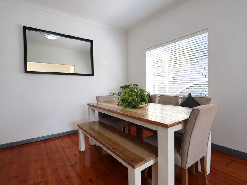 A bright dining room featuring polished timber flooring, crown molding, and a large window with fitted venetian blinds.