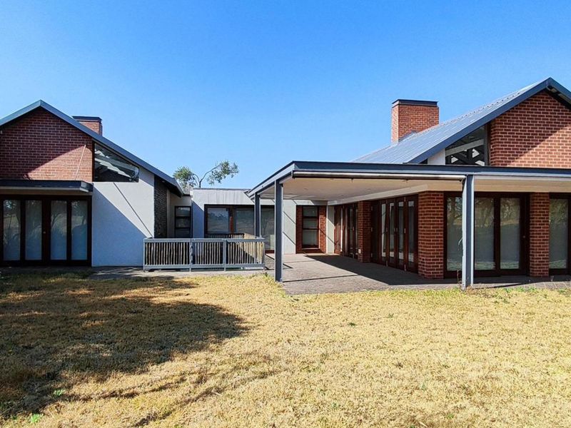Rear view of a modern brick house featuring a covered patio area, large glass sliding doors, and a spacious garden.