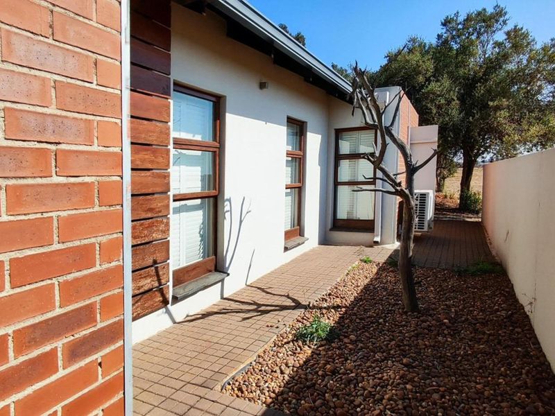 A well-maintained rear exterior view featuring a combination of brick and timber cladding, a paved walkway, and a neat pebble garden bed.