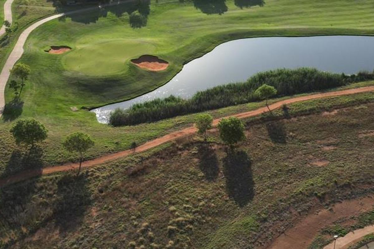 An aerial view of a well-maintained golf course featuring a water hazard, sand bunkers, and a paved cart path.
